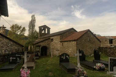 Çan kulesi ve bitişik mezarlığı olan küçük taştan bir kilise. Yumuşak bulutların altında huzurlu bir kırsal alana kurulmuş..