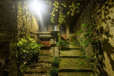 Geceleri sıcacık sokak lambalarıyla aydınlatılmış, taşlarla döşenmiş sessiz bir sokak. Sıcak bir köy restoranına çıkıyor..