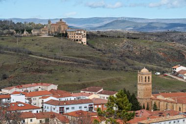 İspanya, Soria 'daki ortaçağ manastırı. Etrafı sarılmış tepelerle çevrili. Önünde tarihi bir kilise ve çan kulesi var..
