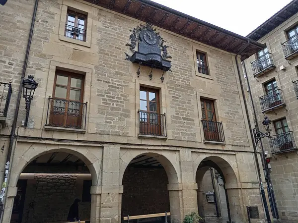 Laguardia, İspanya 'daki tarihi taş bina, kemerli kapılar, ahşap balkonlar ve cephesinde süslü bir demir saat var..