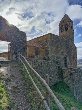 Santa Maria Belediye Başkanı Kilisesi 'nin çan kulesi ve San Vicente de la Sonsierra, İspanya' daki ortaçağ taş duvarları güneş ışığıyla bulutlu bir gökyüzünün altında..