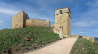 İspanya, San Vicente de la Sonsierra 'daki ortaçağ şatosunun taş kulesi ve kale duvarları mavi gökyüzünün altındaki yeşil bir tepenin üzerinde duruyor..