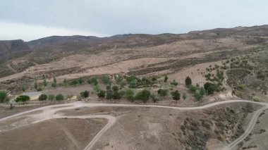 Kurak tepeler ve toprak yollarla çevrili kırsal bir parkın insansız hava aracı görüntüsü.