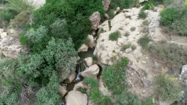Gizli bir şelalenin insansız hava aracı görüntüsü yeşillik ve kayalarla çevrili yeşil bir şelalenin kaya görüntüsü.