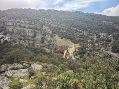 Parque Natural de Despenaperros 'taki yuvarlanan yeşil tepeler ve kayalık uçurumlardan oluşan nefes kesici bir manzara, gökyüzünü dramatik bulutlarla kaplayan..