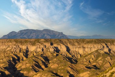 Göz kamaştırıcı bir dağ sırası, ince bulutlu, uçsuz bucaksız mavi gökyüzünün altındaki derin aşınmış kanyonların üzerinde beliriyor.