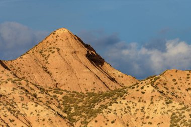 Günün son ışığı, dramatik bulutlu bir gökyüzünün altında çöl dağlarının dokulu sırtlarını vurgular..