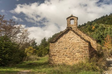 Arka planda canlı orman tepeleri olan pitoresk bir vadiye yerleşmiş, tahta çatılı taştan bir şapel..