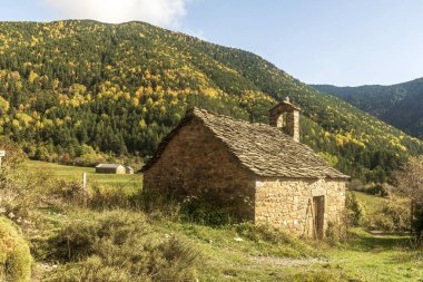 Arka planda canlı orman tepeleri olan pitoresk bir vadiye yerleşmiş, tahta çatılı taştan bir şapel..