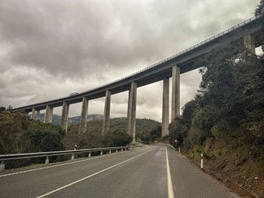 İspanya 'nın Despenaperros kentindeki bir vadi boyunca uzanan büyük beton bir viyadük, uzun sütunlarla desteklenmektedir ve yemyeşil ve dağlarla çevrilidir..