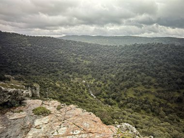Parque Natural de Despenaperros 'taki yuvarlanan yeşil tepeler ve kayalık uçurumlardan oluşan nefes kesici bir manzara, gökyüzünü dramatik bulutlarla kaplayan..