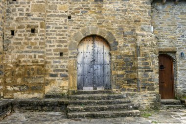 Ağaçlarla çevrili, uzun bir kulesi ve kırsal mimarisi olan antik taş kilise..