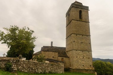 Ağaçlarla çevrili, uzun bir kulesi ve kırsal mimarisi olan antik taş kilise..