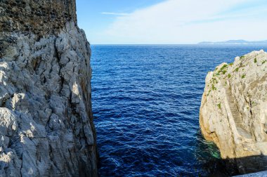Doğal bir kireçtaşı uçurumu berrak gökyüzünün altındaki sakin mavi deniz sularının üzerinde görkemli kuleler.