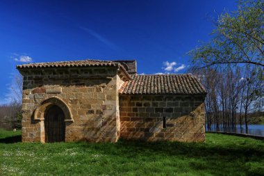 Ağaçlarla çevrili tarihi taş inzivası ve berrak gökyüzü olan su.