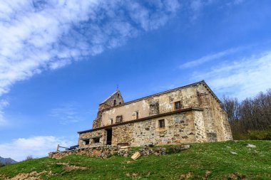 Silindirik kulesi ve tepenin yamacında çan kulesi olan tarihi taş kilise..