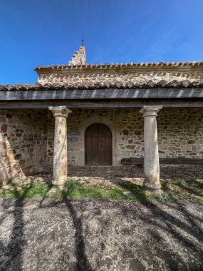 Çimenli tepede kırmızı kiremitli ve ağaçlı geleneksel taş kilise.