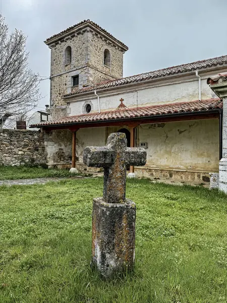 Taş çan kulesi ve yeşil çimlerin üzerinde aşınmış haçı olan tarihi köy kilisesi..