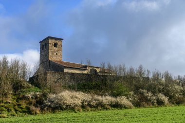 Taş duvarları ve kulesi olan yeşil bir yamaçtaki eski Santa Eulalia kilisesi..