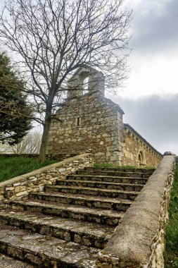 Ojeda Palencia 'nın Micieces de Ojeda bölgesindeki ağaçlarla çevrili çan geçitli ve yıpranmış taş basamaklı eski Roma şapeli.