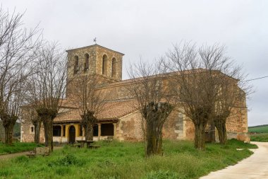 Çan kulesi ve yapraksız ağaçlarla döşenmiş çatısı olan taş kilise..
