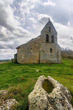 Çan gable ile eski taş kilise ve çimenli arazide kaya oymalı mezar.