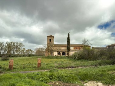 Bulutlu gökyüzünün altında çan kulesi, kemer ve yeşil tarlaları olan Villambroz 'daki Santa Ines Kilisesi