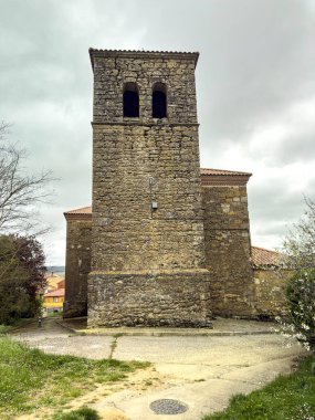 Çan kulesi ve kemerli verandalı, Quintanilla de Osona 'daki ağaçlar ve çitlerle çevrili taş kilise.