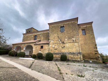 Çan kulesi ve kemerli verandalı, Quintanilla de Osona 'daki ağaçlar ve çitlerle çevrili taş kilise.