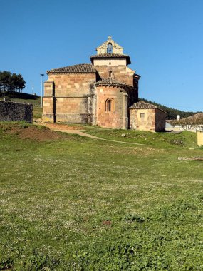Nogales de Pisuerga 'da çift çan kemeri olan, otlar ve ışıkla çevrili Romanca kırsal kilise.
