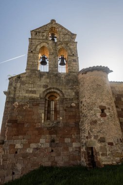 Nogales de Pisuerga 'da çift çan kemeri olan, otlar ve ışıkla çevrili Romanca kırsal kilise.