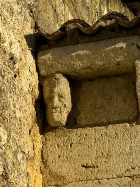 Kilisenin duvarına oyulmuş eski taş bir yüz kısmen çatı kiremitlerinin altına gizlenmiş.