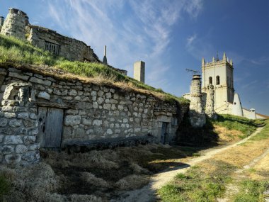 İspanya 'da çimenli bir yamaçtaki tarihi bir kilise kulesinin yanında taşralı yeraltı şarap mahzenleri.