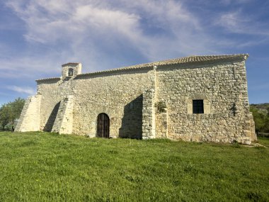 Taş inziva yeri, dramatik mavi ve beyaz gökyüzünün altında çimenli kırlarda tek başına duruyor.