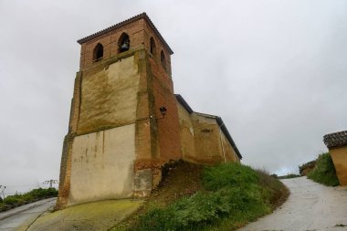 Kemerli çan pencereleri, sıva yüzeyleri ve görünür tuğlaları olan eski kırsal kilise kulesi.