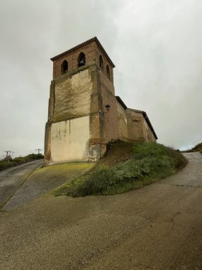 Kemerli çan pencereleri, sıva yüzeyleri ve görünür tuğlaları olan eski kırsal kilise kulesi.
