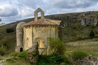 Taş duvarları ve kırsal bir dağ manzarasında kiremitli çatısı olan tarihi Roma kilisesi.