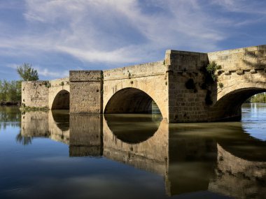 Nehir yüzeyinde yansıyan büyük kemerli antik taş köprü.