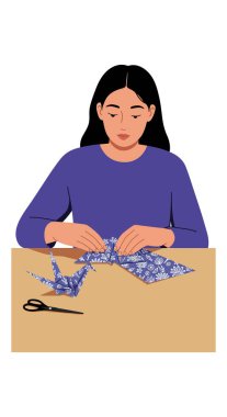 Mavi desenli kağıt vinç origamisi yapan bir kadın tasviri. Masada makaslı, sakin ve odaklanmış bir ruh hali..