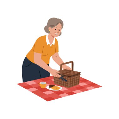 Yaşlı bir kadın piknik sepetini kırmızı kareli battaniyeyle çay ve kurabiyelerle hazırlıyor..