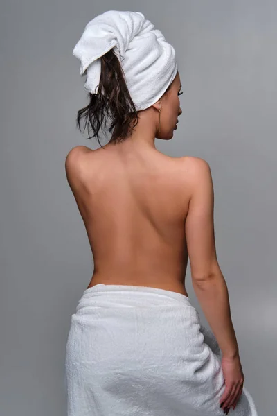 年轻迷人的黑发女人洗完澡后用白色毛巾盖住头和臀的照片 后视镜 摄影棚拍摄 — 图库照片