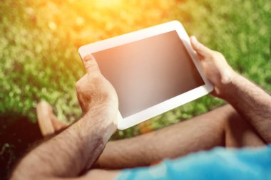 Casual giyimli genç adam parkta otururken modern dijital tablet kullanarak close-up, yenilikçi bağlantı sosyal ağ dışında güneş ışığı dostum. Güneş parlaması