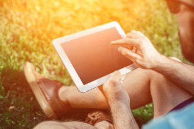 Casual giyimli genç adam parkta otururken modern dijital tablet kullanarak close-up, yenilikçi bağlantı sosyal ağ dışında güneş ışığı dostum. Güneş parlaması
