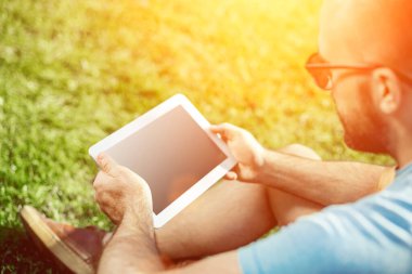 Casual giyimli genç adam parkta otururken modern dijital tablet kullanarak close-up, yenilikçi bağlantı sosyal ağ dışında güneş ışığı dostum. Güneş parlaması