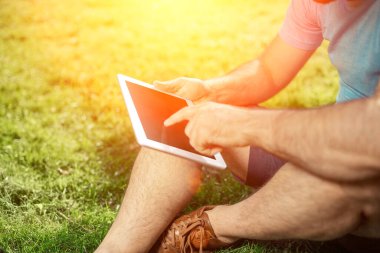 Parkta oturan ve modern dijital tablet, tablet pc dışında sosyal ağ kavramı kullanarak erkek blogger kullanarak genç hippi çocuk. Güneş parlaması