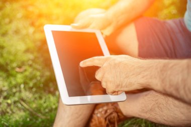 Parkta oturan ve modern dijital tablet, tablet pc dışında sosyal ağ kavramı kullanarak erkek blogger kullanarak genç hippi çocuk. Güneş parlaması
