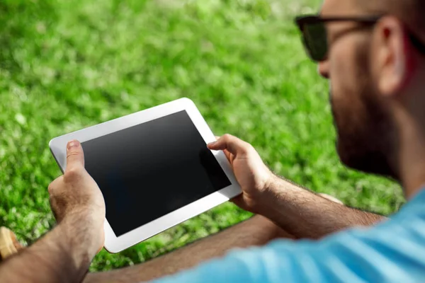 stock image Young man using and typing tablet computer in summer grass. Freelancer working in outdoor park