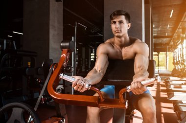 Yük altındaki ellerin gergin kasları. Spor salonunda pazılar için egzersiz yapan bir adam. Simülatördeki kaslara çalış. Spor dergileri, posterler ve web siteleri için fotoğraflar. Güneş parlıyor
