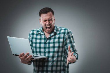 Ekose gömlek giyen, dizüstü bilgisayar kullanan yakışıklı bir adamın portresi. Stüdyo çekimi. Duygular