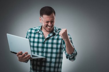 Ekose gömlek giyen, dizüstü bilgisayar kullanan yakışıklı bir adamın portresi. Stüdyo çekimi. Duygular